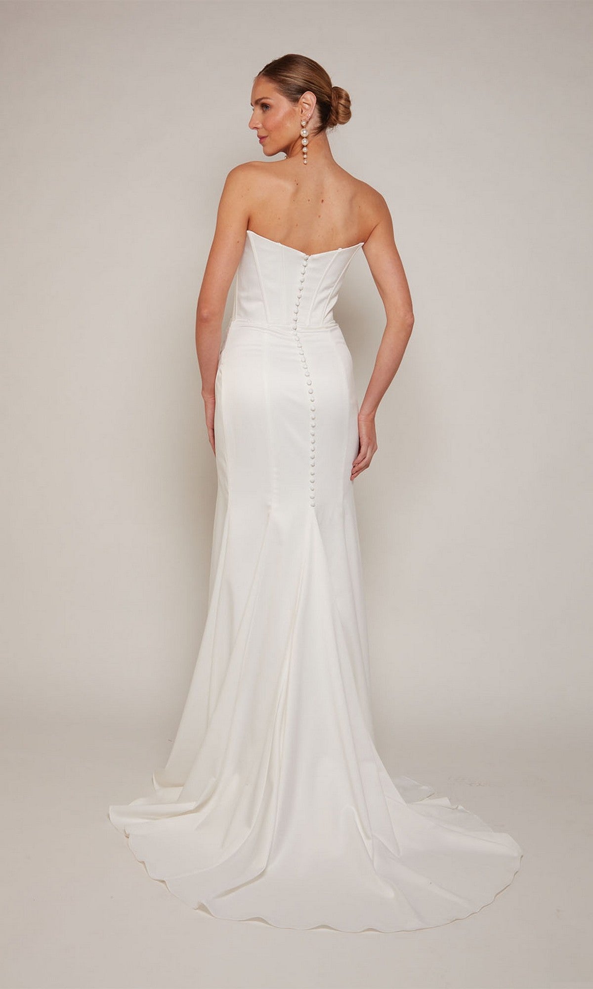 A woman models the Alyce 7093 long formal dress, featuring a strapless satin bodice, button-back detail, and a flowing sheath skirt with train—an elegant choice for formal occasions—against a simple backdrop.